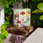 Zestaw herbat Basilur Vintage Blossoms w prezentowym, zielonym pudełku na stole z kwiatami.